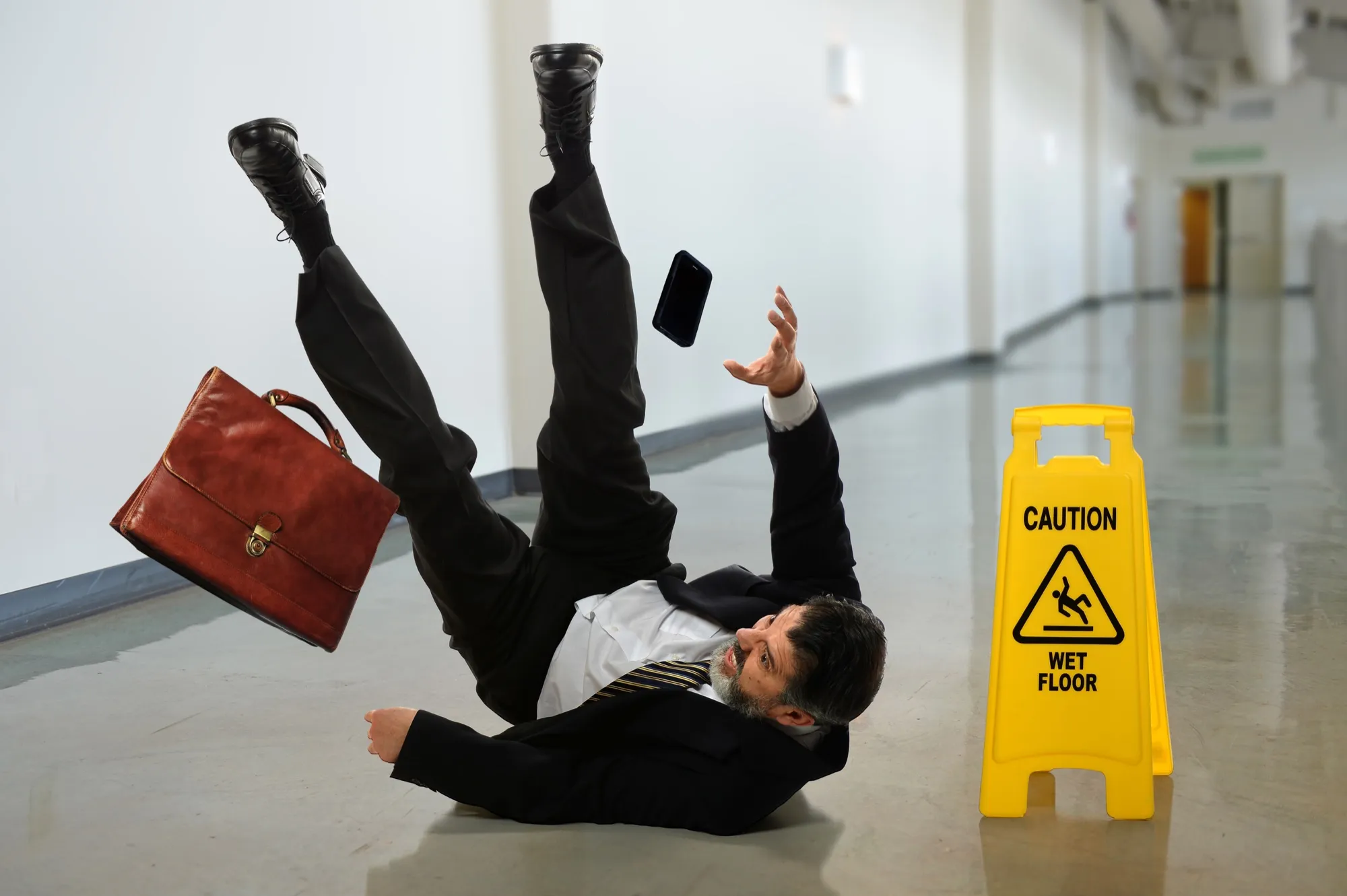 Businessman slipping on a wet hallway floor next to a caution sign